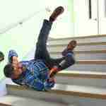 Worker falling backwards down steps with a power drill in hand whilst attempting to protect head with an outstretched arm