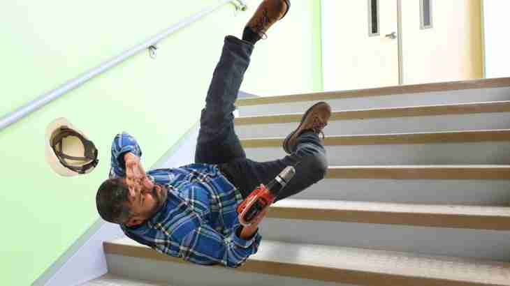 Worker falling backwards down steps with a power drill in hand whilst attempting to protect head with an outstretched arm