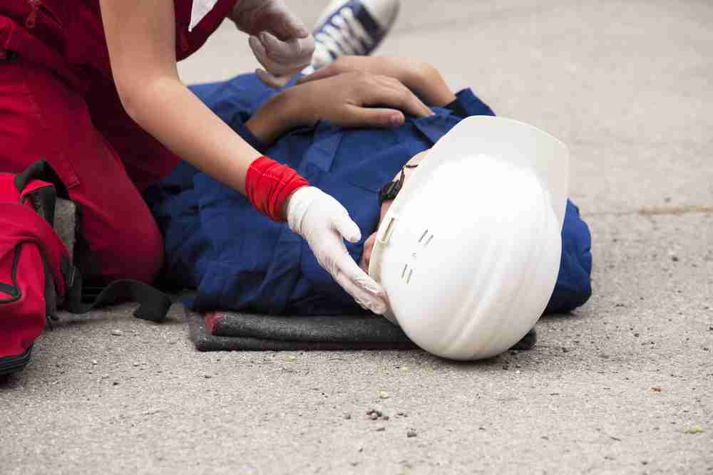 Injured worker wearing a helmet lying on the ground while first aider supports their head after a concussion