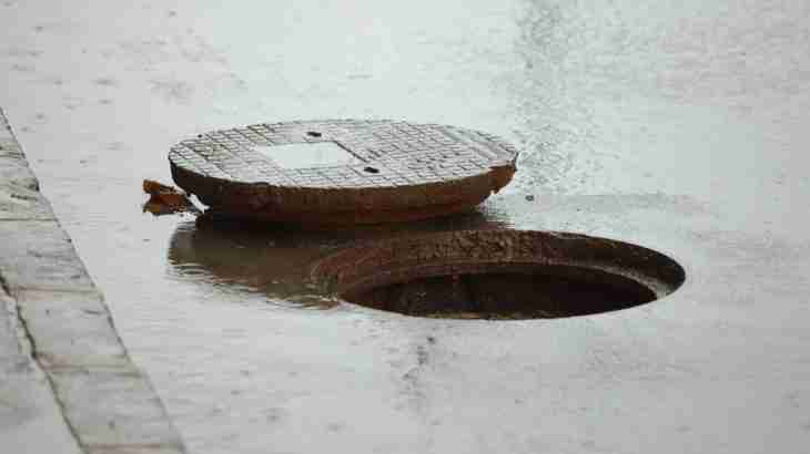 Defective manhole cover displaced above road surface leaving an open hole and serious trip hazard