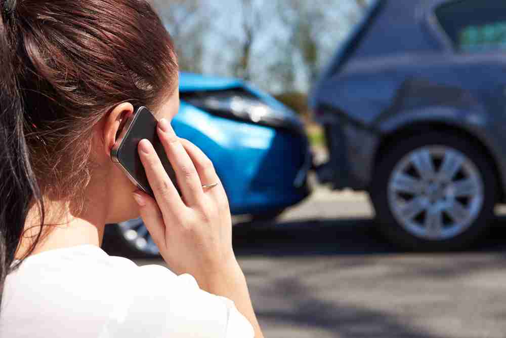 Driver on the phone facing two cars that have collided on a road driver notifying police and motor insurer following accident