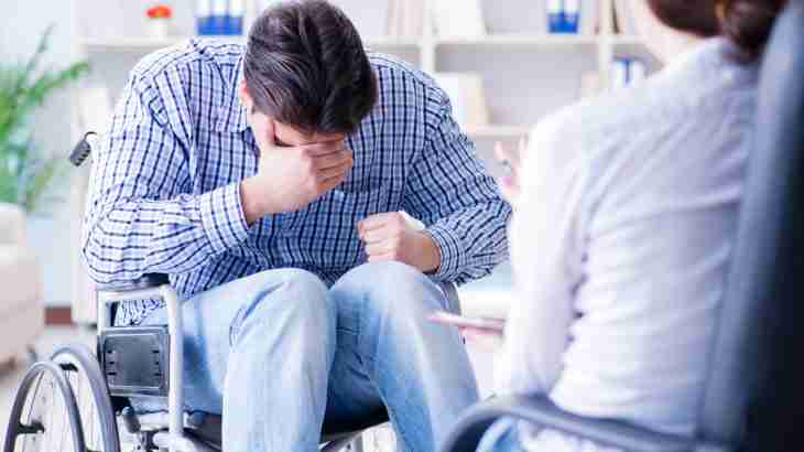 Accident victim in wheelchair at doctors covering face with hand to conceal facial fracture injury