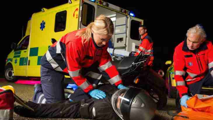 Motorcyclist lying on a road receiving assistance from two paramedics with an ambulance waiting nearby