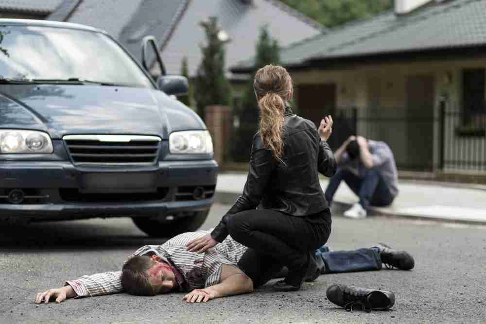 Head & Brain Injury Claims Man with head injury lying on the road after a car accident while bystanders assisting