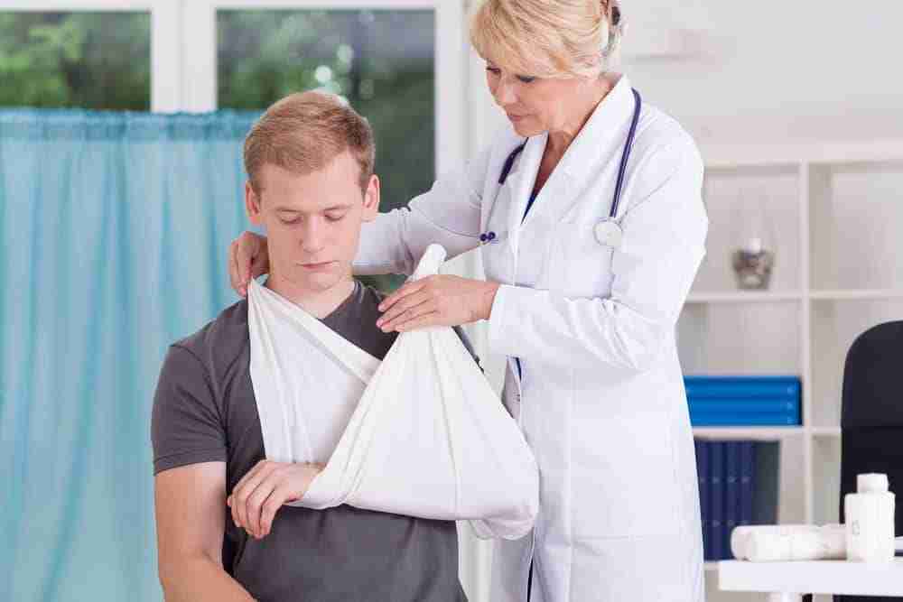 Joint Dislocation Claim Patient sitting in a hospital ward with arm in a sling while a doctor provides treatment
