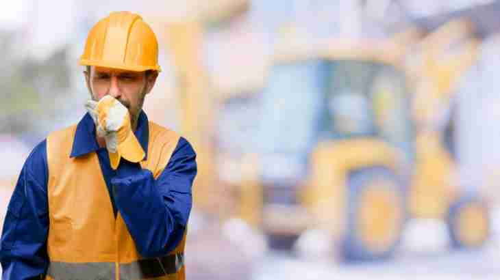 Worker in protective gear coughing due to lung disease from workplace exposure