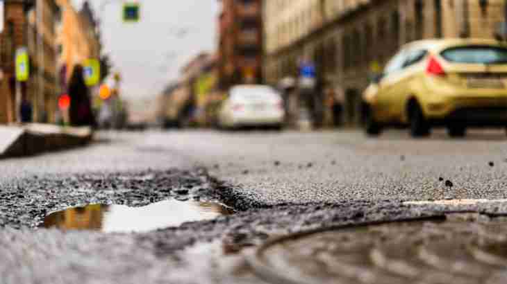 Pothole in a road near a manhole cover creating a trip hazard that could cause a fall accident