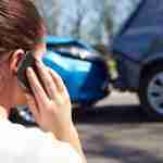 Woman at a road accident scene calling on her phone with two collided cars in the background