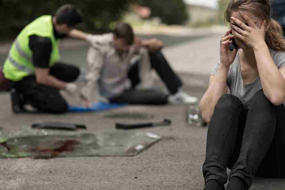 Man injured in a road accident being assisted by a medic while a woman nearby makes a phone call