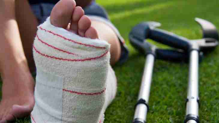 Person sitting on grass with lower leg and foot in plaster and crutches nearby following a serious shattered ankle injury