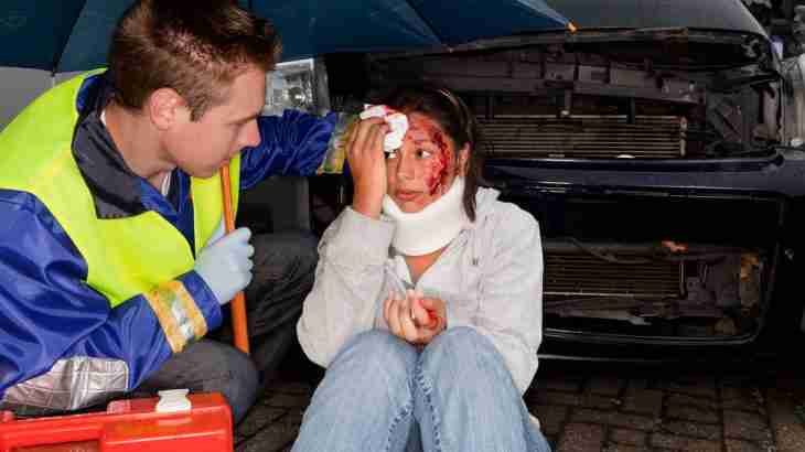 Injured person receiving treatment from a paramedic following an accident, with facial injuries and a neck brace visible