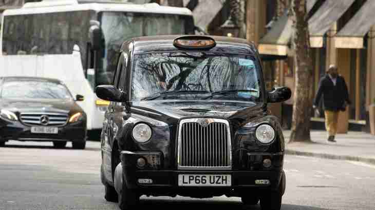 Black cab taxi driving on a road with pedestrians and other vehicles nearby