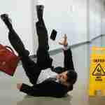 Man in suit slipping on a wet floor and falling with belongings in the air during a slip trip fall accident