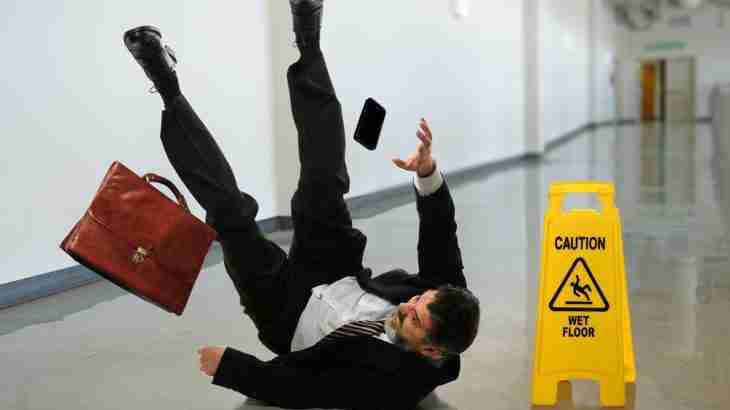 Man in suit slipping on a wet floor and falling with belongings in the air during a slip trip fall accident