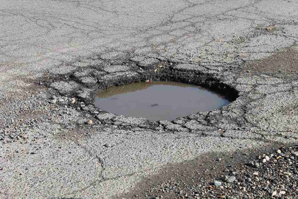 Large deep pothole in road presenting a trip hazard for pedestrians Deep pothole in road presenting a tripping hazard for pedestrians