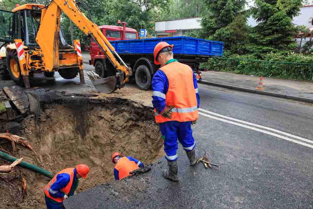 Unprotected excavation hole in road showing hazard for pedestrians and road users. Council workers inside an unprotected road works excavation hole with no barriers creating a serious hazard