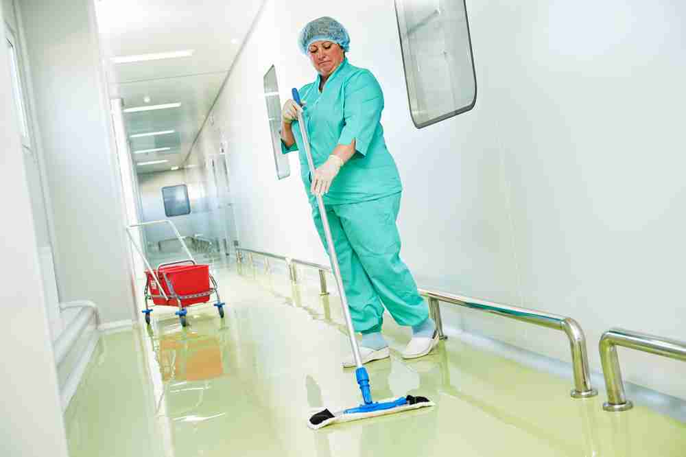 Hospital worker mopping a wet floor in a corridor creating a slip hazard for pedestrians